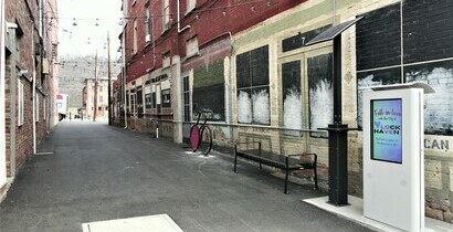 Image showing Fallon Alley, with a bench, a bike rack, a solar charging station, and a digital kiosk on the right side of the image, with cafe lights going down the alley.